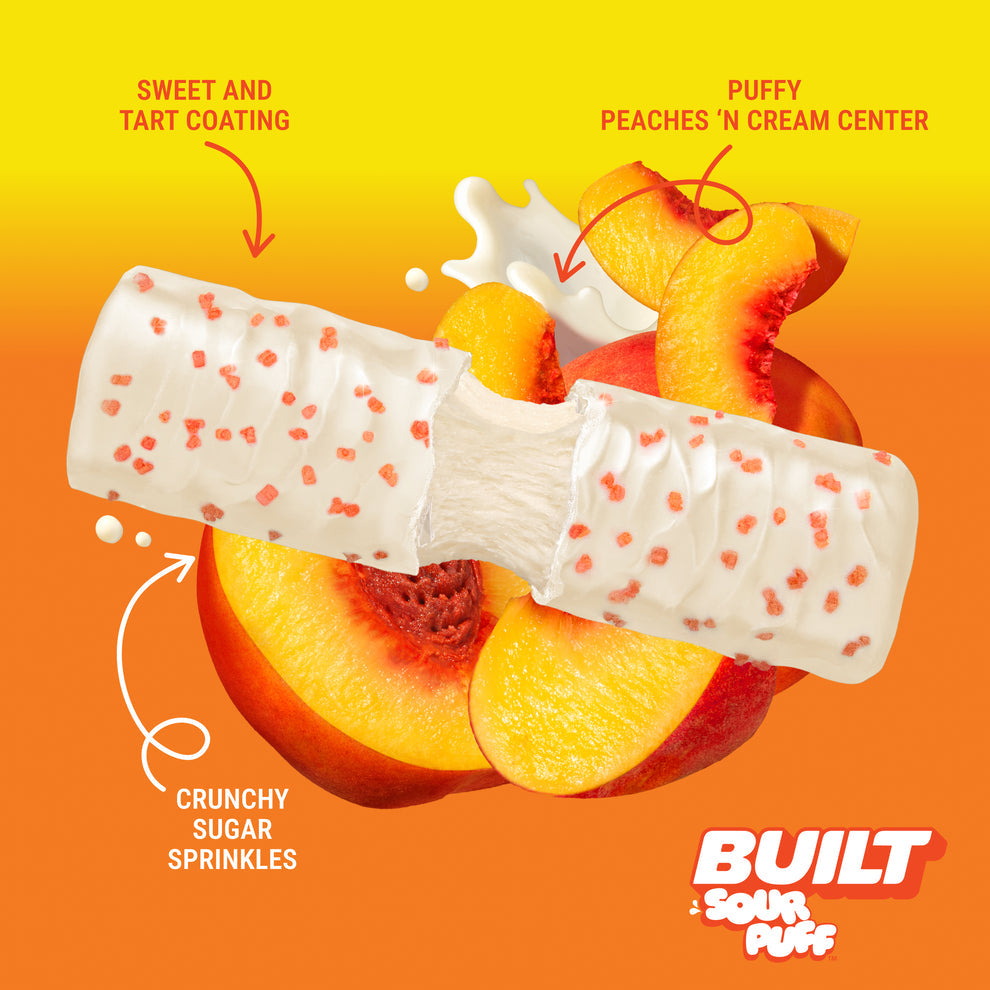 Built Bar Puffs Canada – Sour Puff Sweet Peach Punch Protein Bar 40g partially unwrapped showing white chocolate coating with crunchy sugar sprinkles and puffy peach'n cream center on orange background