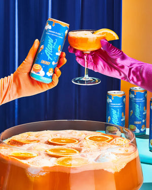 Two hands in colorful gloves holding a can and a cocktail glass with orange slices, surrounded by more cans and a punch bowl filled with orange-themed drinks.