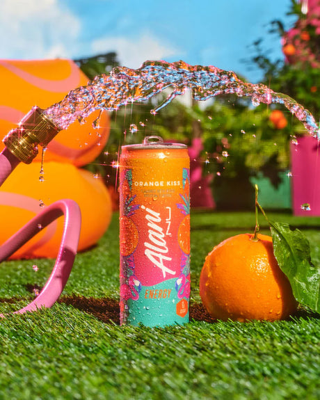 Alani energy drink can with colorful design on grass, surrounded by orange and pink elements.